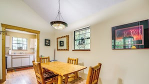 A wooden dining table with cushioned chairs, a kitchen in the background, and a framed artwork on the wall. - 2 Mi to Parkway! Pet-friendly Cabin w/ Hot Tub (Sevierville)