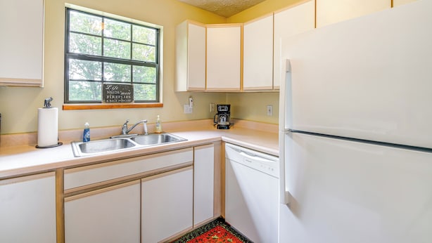 A compact kitchen with white cabinets, a dishwasher, a coffee maker, and a window with a view of trees. - 2 Mi to Parkway! Pet-friendly Cabin w/ Hot Tub (Sevierville)