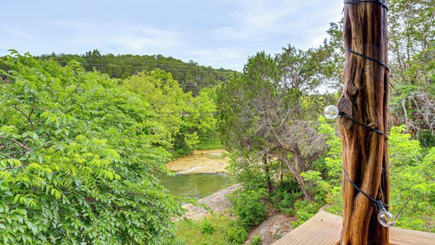 Eine Holzterrasse mit Blick auf einen Fluss, üppigem Grün und eine entfernte Hügelkette.