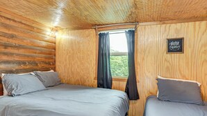 Ein Zimmer in einer Holzhütte mit zwei Betten, einem Fenster mit Vorhängen und einem Schild an der Wand.