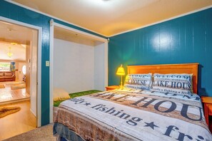 A room with a bed, a nightstand, a lamp, and a door leading to another room.