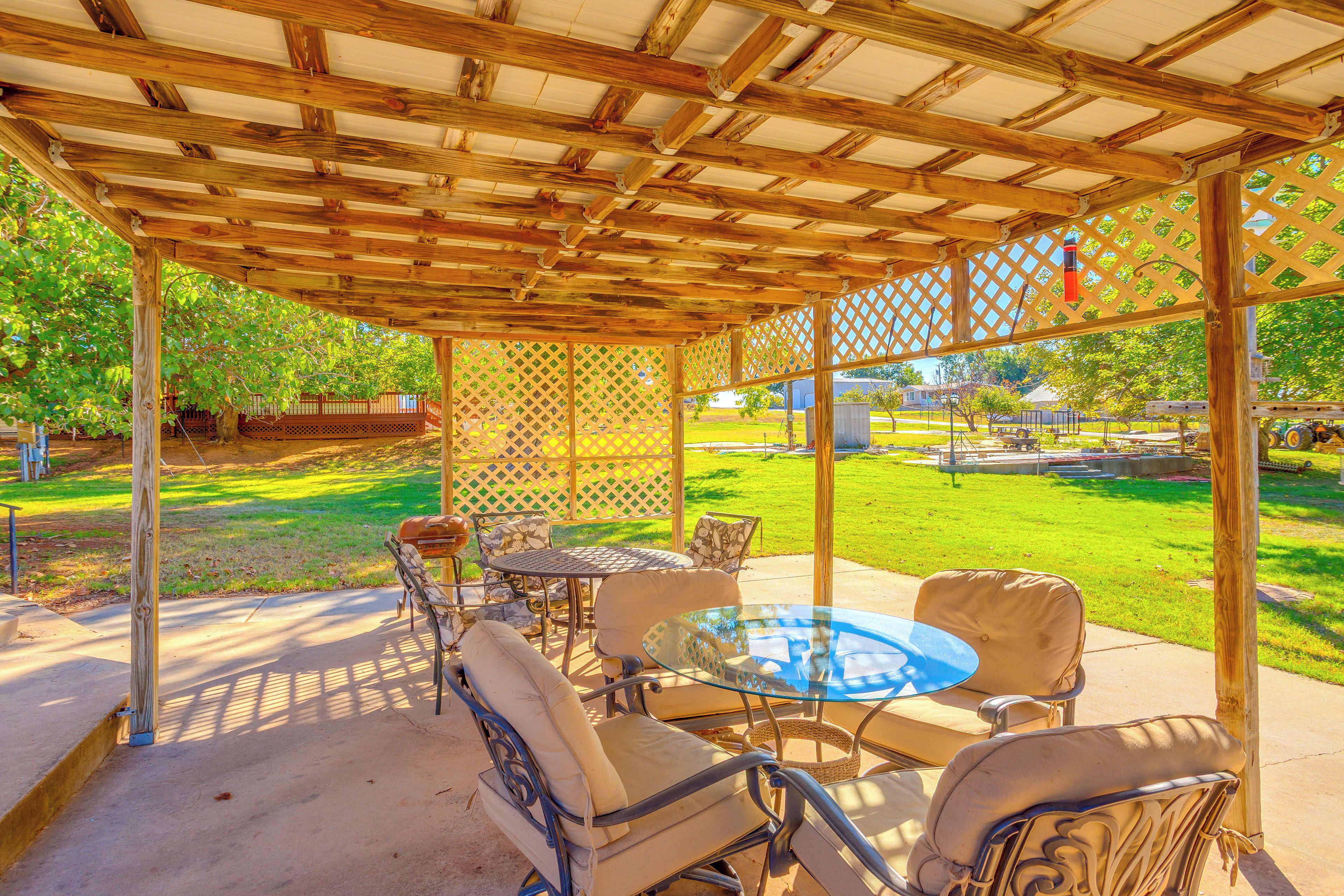 A covered patio area with a table and chairs, a grill, and a view of a grassy yard.