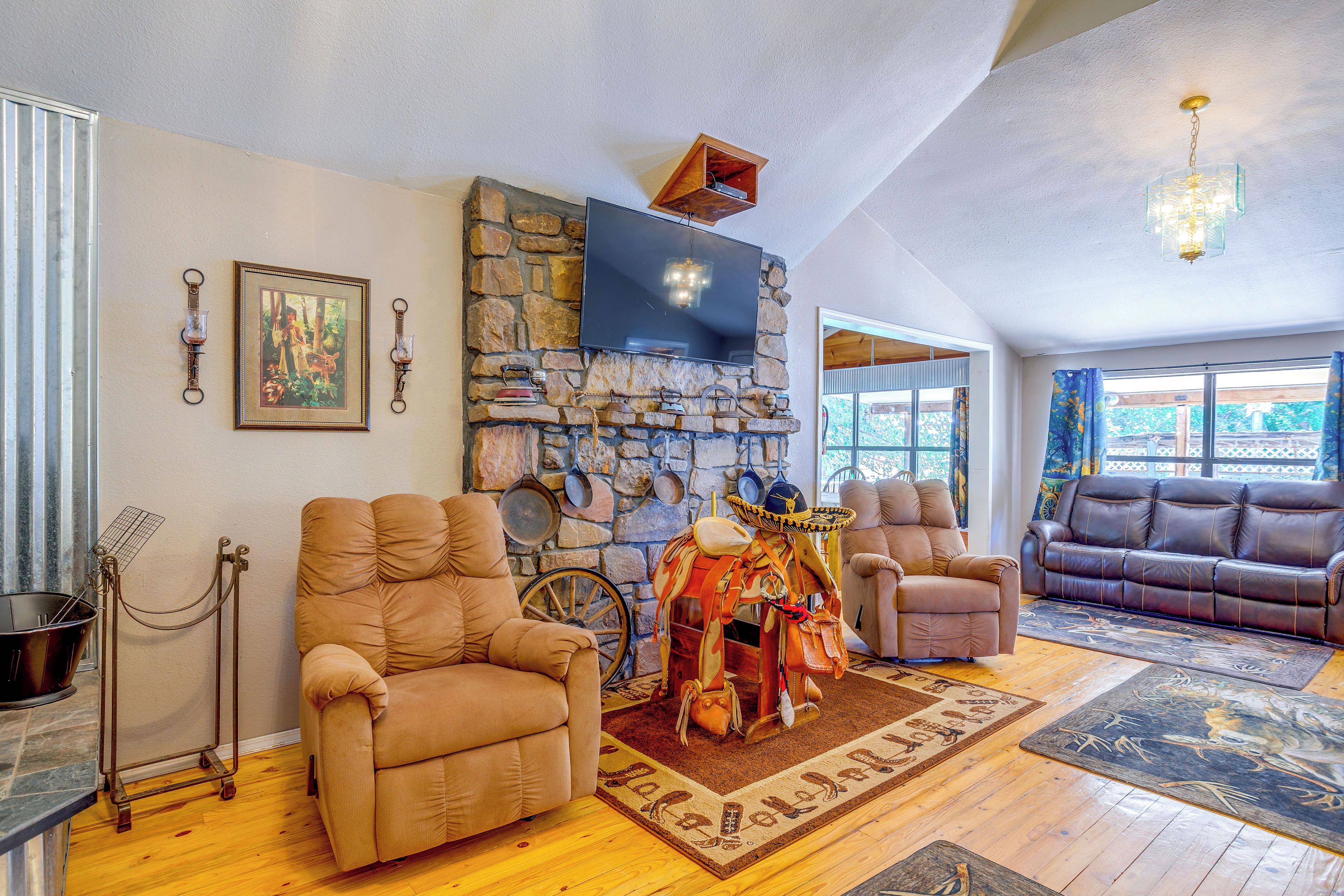 A spacious living room with a stone fireplace, multiple seating options including a recliner and a sofa, and a large flat-screen TV mounted above the fireplace.