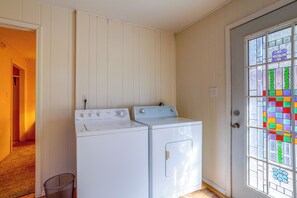 A laundry room with two stacked washers and dryers, a door with stained glass, and a hallway leading to another room.