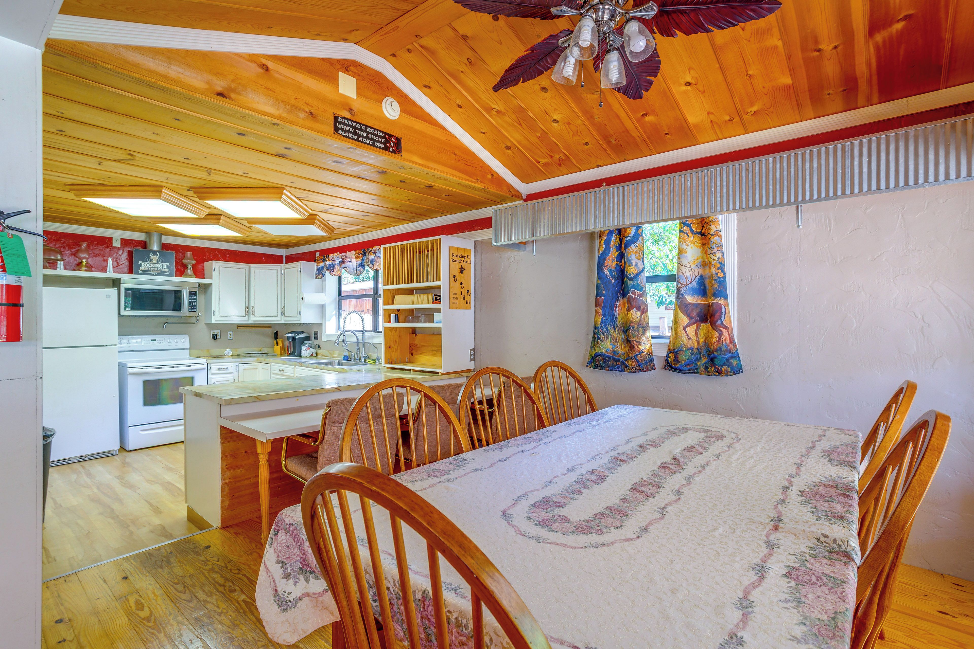 A kitchen with a microwave, stove, and cabinets, a dining area with a table and chairs, and a ceiling fan.