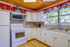 A kitchen with white cabinets, a stove, a microwave, and a window with a view of trees. - Rustic Home w/ Patio, 1 Mi to Sunset Beach! (Butler)