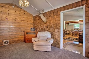 A room with a wooden wall, a mounted deer head, a plush armchair, a small wooden cabinet, and a fan.