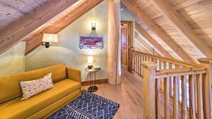 Une pièce mansardée chaleureuse avec un plafond en bois, un canapé jaune, un tapis à motifs et un escalier avec des rampes en bois.