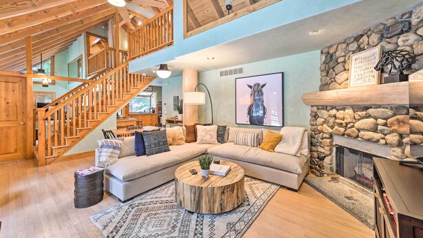 Un salon spacieux avec un escalier en bois, une cheminée en pierre et un grand canapé d’angle.