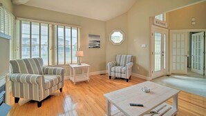 A spacious living room with striped armchairs, a coffee table, and a view of the beach through large windows. - Spacious Brigantine Home ~ 1 Block to Beach! (Brigantine)