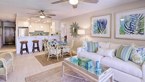 A spacious living room with a white sofa, a coffee table, and a dining area with chairs and a table. There is a kitchen in the background with white cabinets and a refrigerator. - Tropical St. Thomas Resort Getaway w/ Pool Access! (St. Thomas)