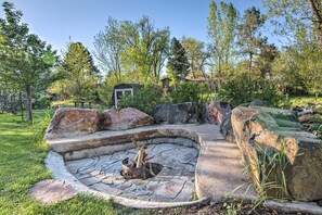 A stone fire pit surrounded by large rocks and a grassy area with trees and a small shed in the background. - 11 Mi to Denver Zoo: Lakewood Studio w/ Fire Pit! (Lakewood)