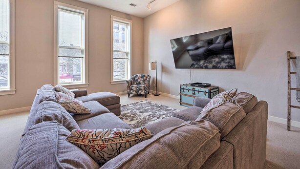 A living room with a large sectional sofa, a flat-screen TV mounted on the wall, and a patterned rug. - Charming Dtwn Holland Escape: Above Crust 54! (Holland)