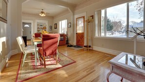 A spacious room with hardwood floors, a dining area with a table and chairs, a large window with a view, and a ceiling fan. - 'the Diamond Bungalow' - Cozy Caldwell Home! (Caldwell)