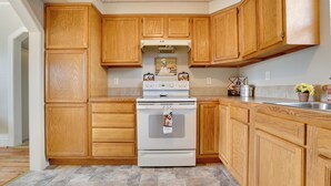 A kitchen with wooden cabinets, a white stove, and a tiled floor. - 'the Diamond Bungalow' - Cozy Caldwell Home! (Caldwell)