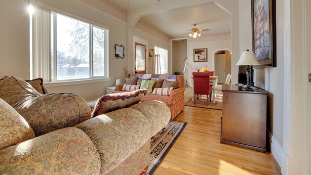 A spacious living room with a large sofa, a dining area with a red chair, and a small cabinet. - 'the Diamond Bungalow' - Cozy Caldwell Home! (Caldwell)