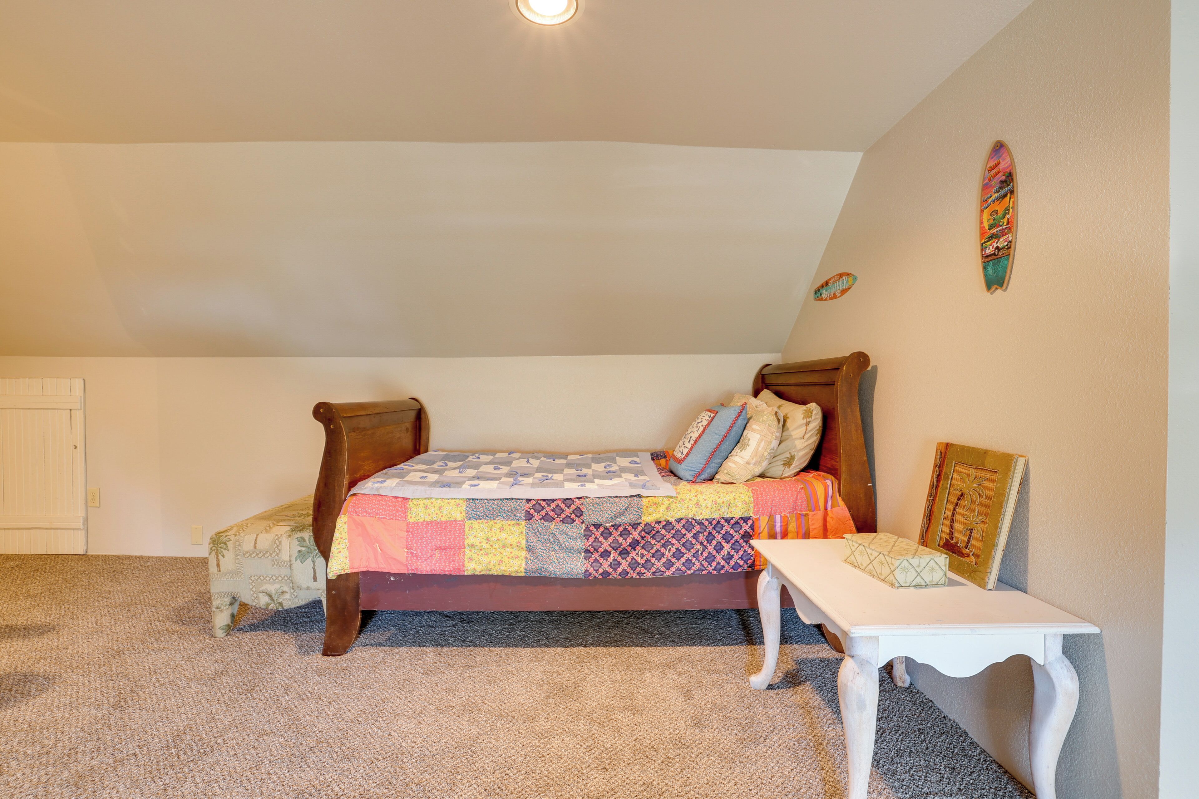 A bedroom with a bed, a small table, and a wall with a surfboard decoration.