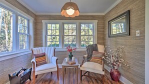 Une pièce dotée de trois grandes fenêtres, d’un plancher en bois et de deux fauteuils blancs ornés de coussins à rayures.