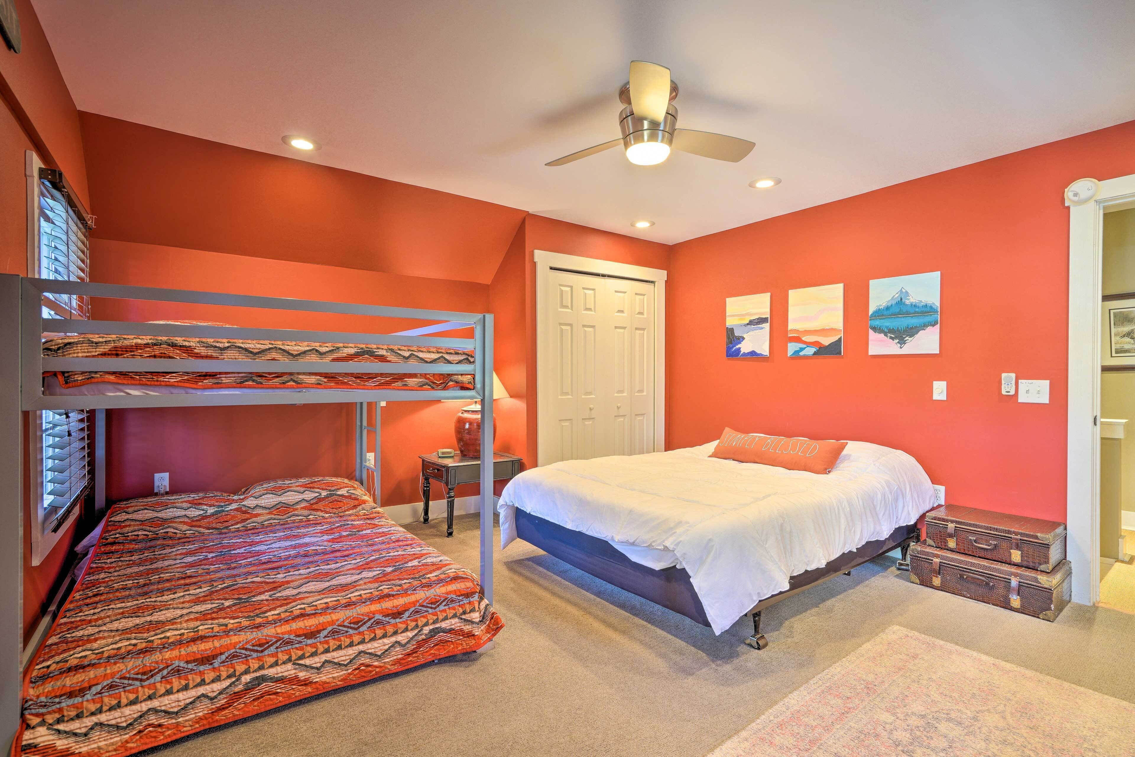 A bedroom with a bunk bed, a single bed, a ceiling fan, and artwork on the wall.