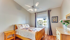 A bedroom with a wooden bed, a nightstand, a dresser, a ceiling fan, and a window with curtains. - Private Patio & Grill: Lakefront Chandler Home (Chandler)