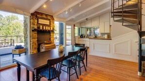 A modern kitchen with a stone fireplace, a dining area with a wooden table and chairs, and a spiral staircase.
