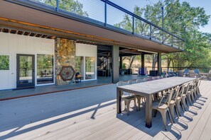 Um terraço ao ar livre com uma mesa comprida e cadeiras, uma parede de pedra e uma área coberta com guarda-corpo.
