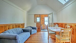 A room with a wooden floor, a blue sofa, wooden dining table with chairs, and a skylight. - Lakefront Rumney Retreat w/ Shared Dock & Beach! (Rumney)