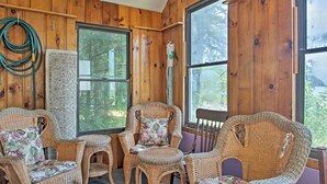 A cozy room with wooden walls and large windows, wicker furniture, and a visible garden outside. - Lakefront Rumney Retreat w/ Shared Dock & Beach! (Rumney)