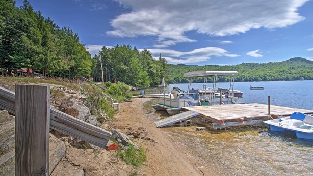 A lakeside dock with boats, a wooden pier, and a forested area. - Lakefront Rumney Retreat w/ Shared Dock & Beach! (Rumney)