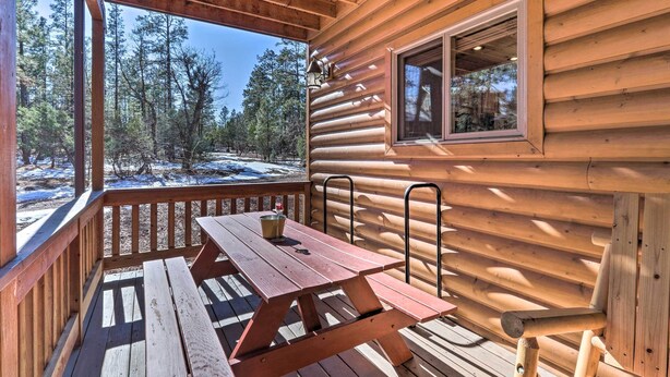 A wooden cabin with a deck, a picnic table, and a window overlooking a snowy forest.