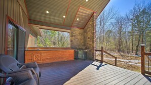 A covered outdoor deck with wicker chairs, a stone fireplace, and a view of the forest. - Ouachita Mtn Home: Near ATV & Hiking Trails! (Hodgen)