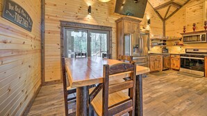 A wooden interior with a dining table and chairs, a kitchen with appliances, and a large window. - Ouachita Mtn Home: Near ATV & Hiking Trails! (Hodgen)