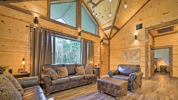 A cozy log cabin interior with a leather sofa, ottoman, and a fireplace. - Ouachita Mtn Home: Near ATV & Hiking Trails! (Hodgen)