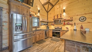 A modern kitchen with wooden walls, stainless steel appliances, and a stone accent wall. - Ouachita Mtn Home: Near ATV & Hiking Trails! (Hodgen)