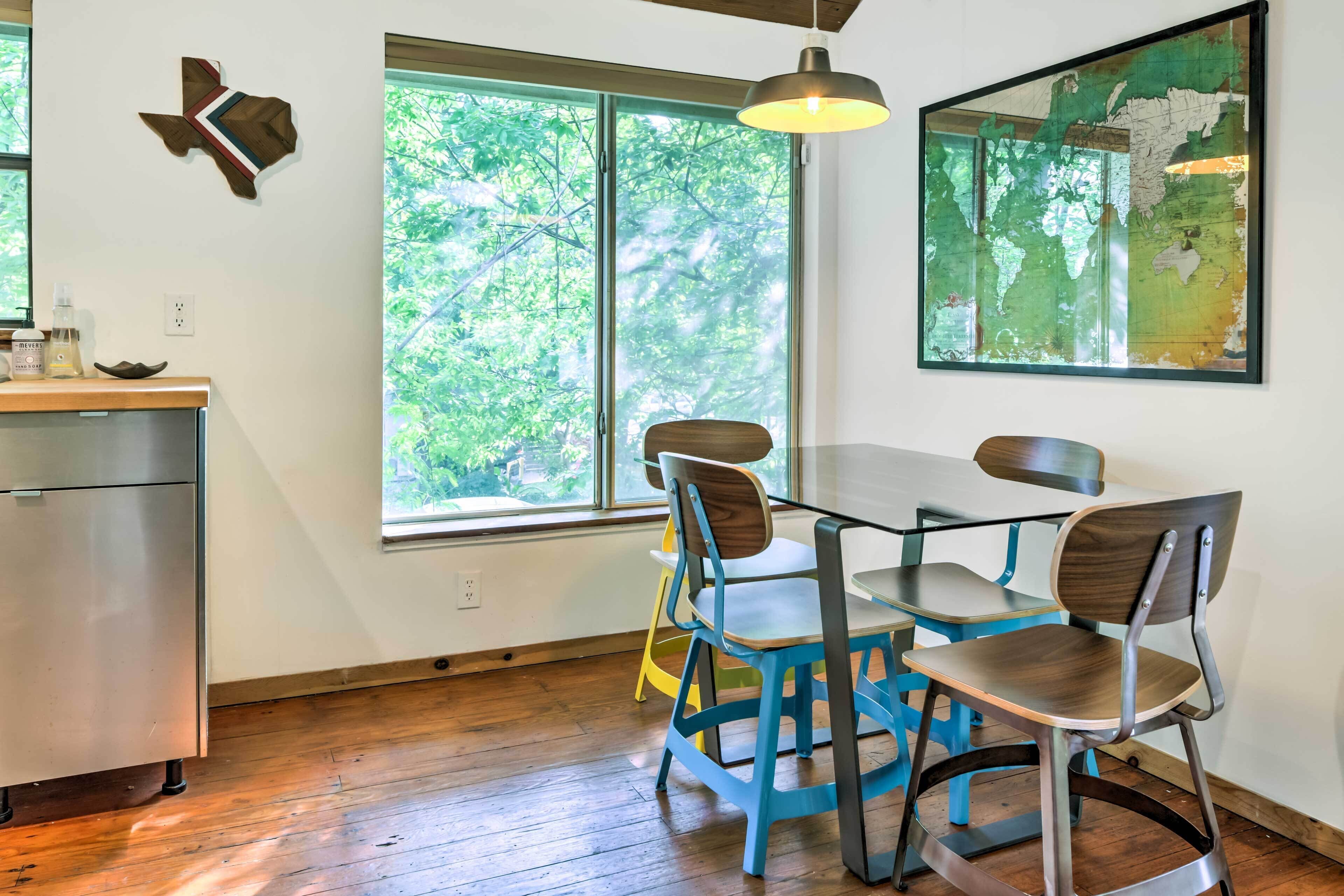 Un coin repas avec une table et des chaises en bois, une carte accrochée au mur et une vue sur les arbres par la fenêtre.