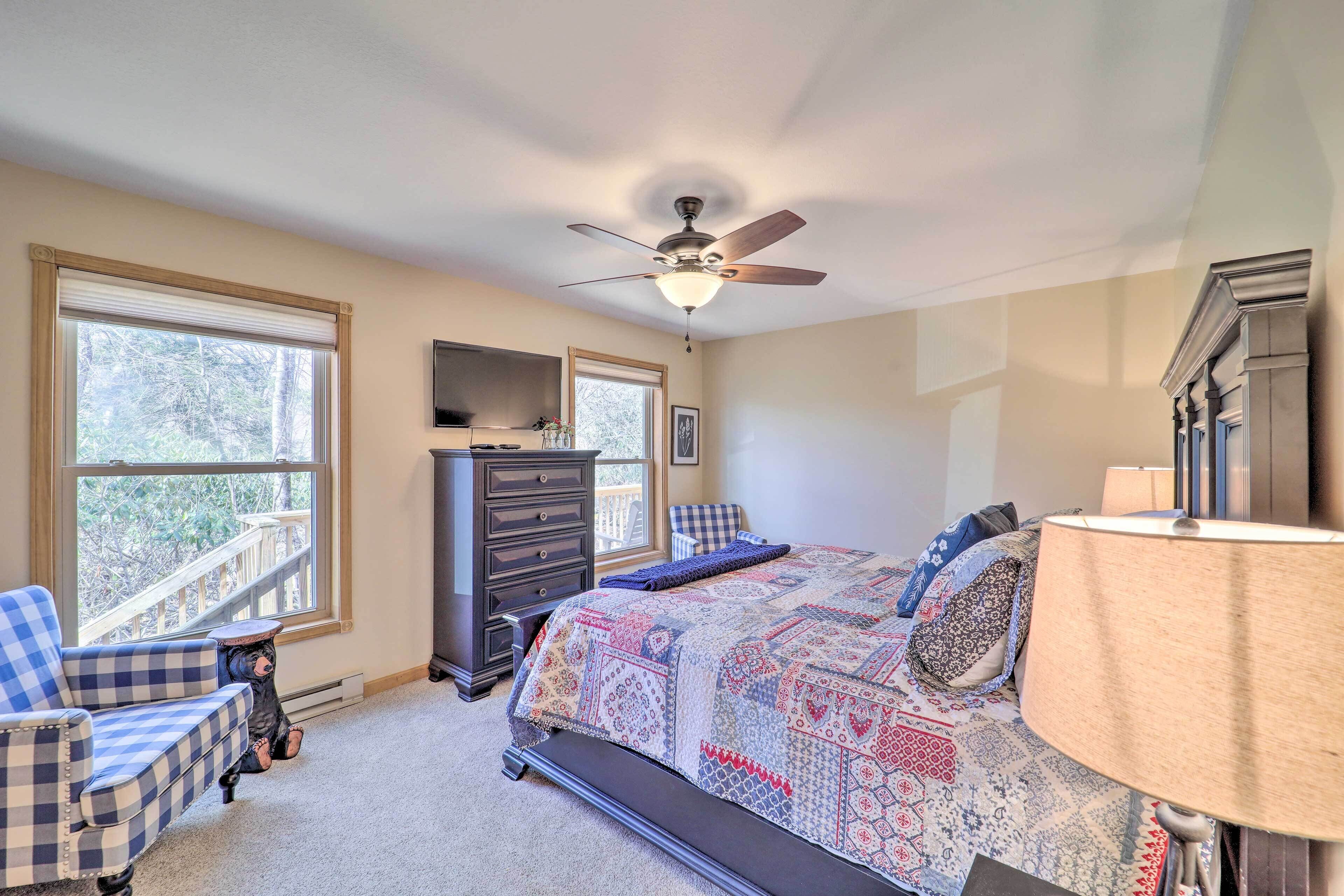 A bedroom with a bed, a dresser, a chair, a ceiling fan, and large windows.