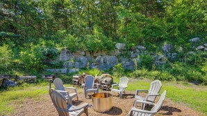 Un foyer entouré de fauteuils Adirondack, dans un cadre naturel agrémenté d’un mur de pierres et de verdure.