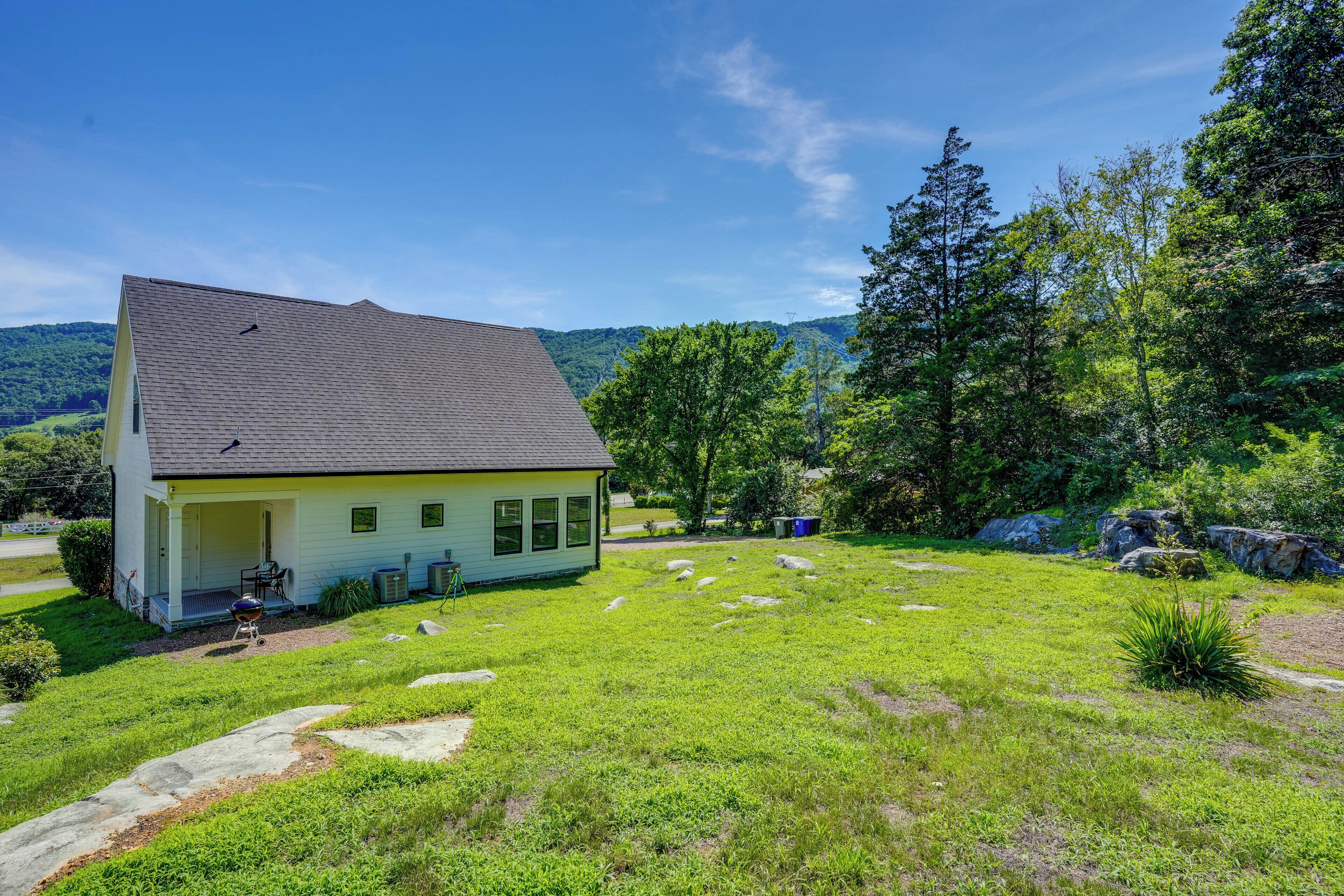 A house with a sloped roof, a porch, and a grassy yard with rocks and trees.