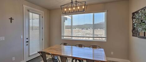 A dining area with a wooden table and metal chairs, a chandelier, a window with blinds, and a door with a doormat.
