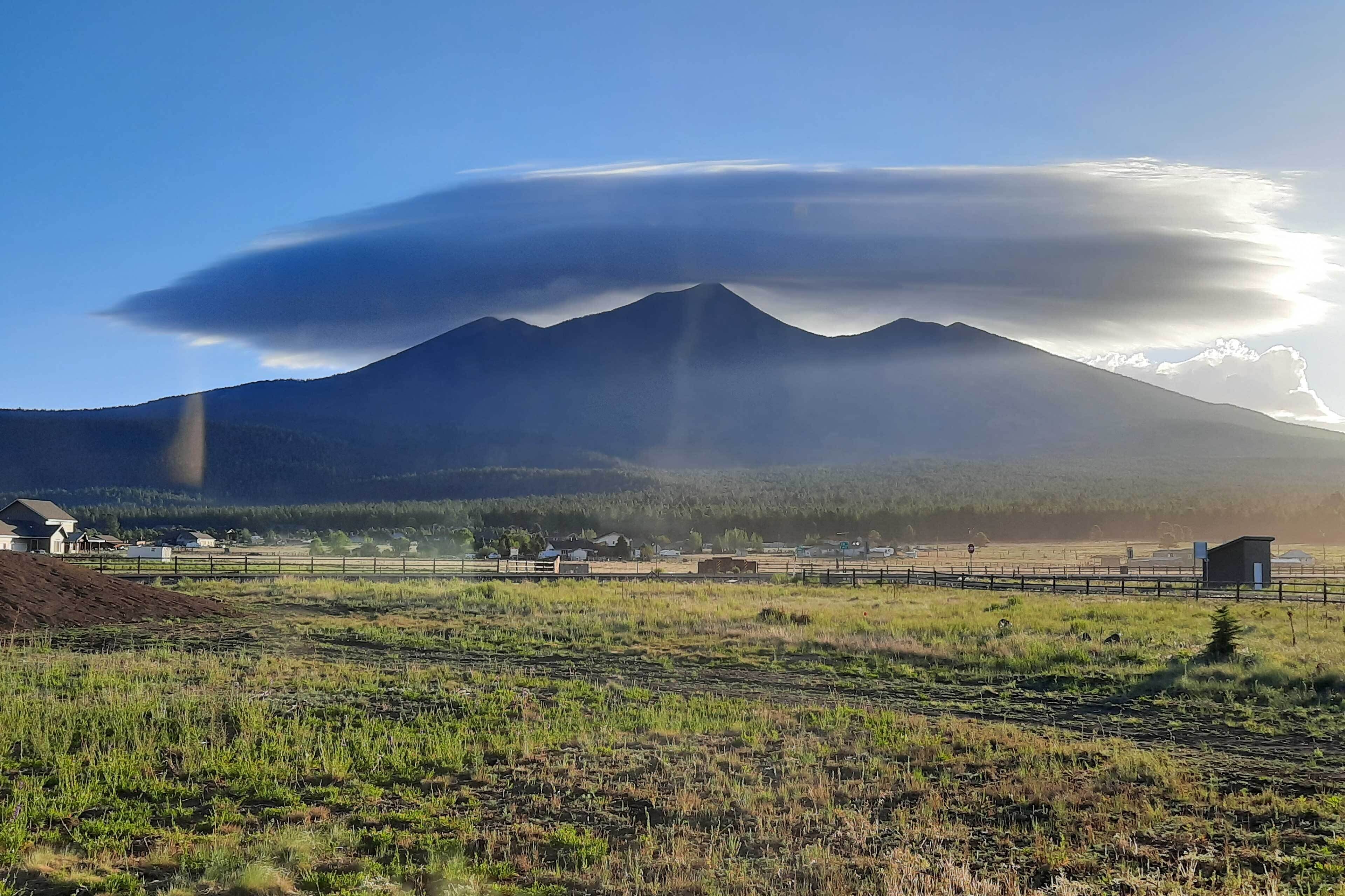 Un paysage de montagne avec un ciel dégagé, une clôture et un petit bâtiment au premier plan.