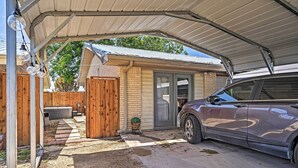 Eine überdachte Garage mit einem Auto darin, ein Holzzaun und ein kleines Topfgepflanzte.