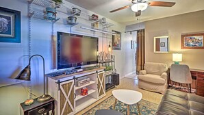 Ein Wohnzimmer mit Fernseher, Sofa, Sesseln, einem Couchtisch, einem Deckenventilator und Regalen mit Dekoration.