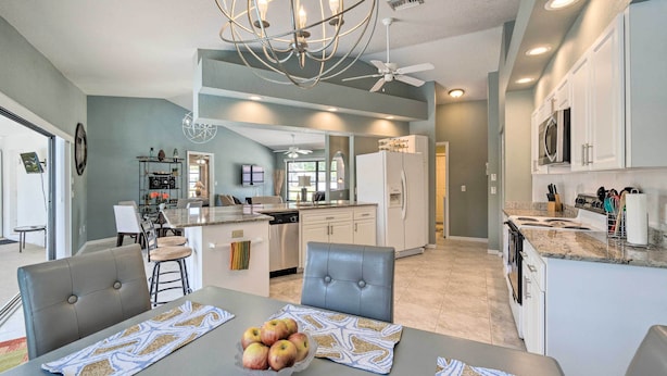 A modern kitchen with a central island, white cabinets, and a dining area with a table set for four. - Modern House < 5 Miles to Port Charlotte Beach! (Port Charlotte)