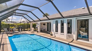 A swimming pool with a glass enclosure, surrounded by lounge chairs and a patio area. - Modern House < 5 Miles to Port Charlotte Beach! (Port Charlotte)