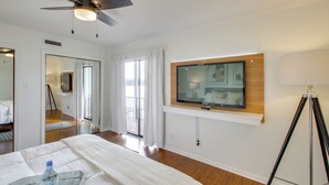 A hotel room with a bed, a TV mounted on the wall, a ceiling fan, and a large window with curtains. - Sunset-view Resort Condo on Lake Hamilton! (Hot Springs)