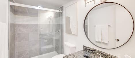 Une salle de bain moderne avec une douche à parois de verre, des toilettes, un lavabo et un grand miroir.