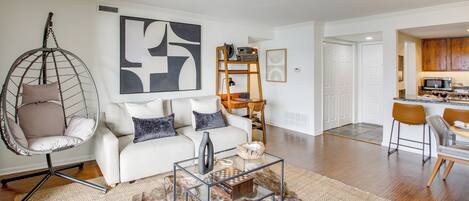 Un salon moderne avec un fauteuil suspendu, une table basse en verre et un canapé blanc.