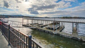 A dock area with boats, a covered seating area, and a view of the water and distant hills. - Sunset-view Resort Condo on Lake Hamilton! (Hot Springs)