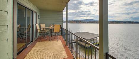 A balcony with a view of a lake, a dining table with chairs, and a doormat.