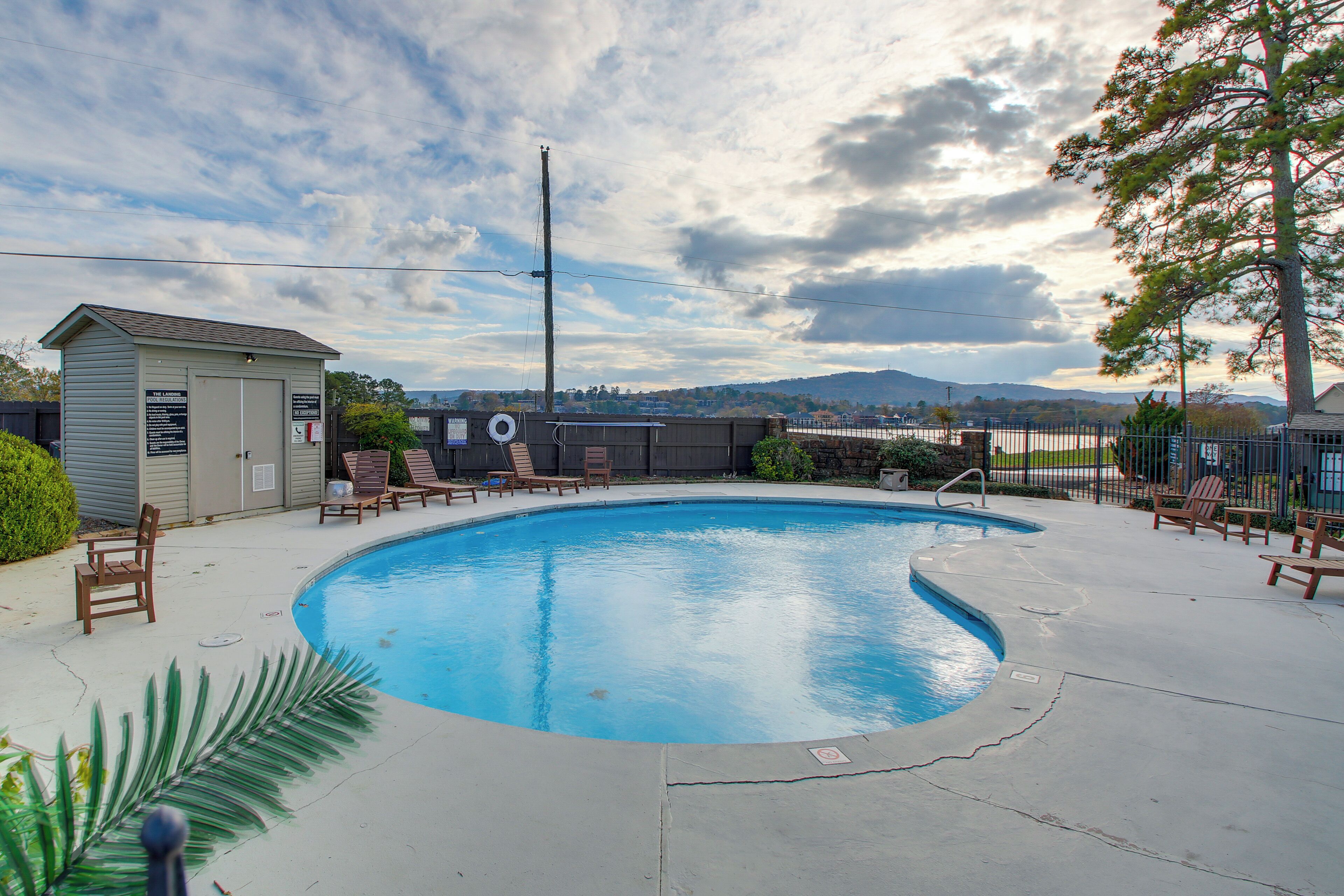 Une piscine avec des chaises longues, un petit abri de jardin et une vue sur des collines lointaines.
